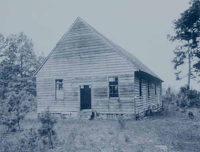 Archival photograph of a plain wood-frame country meeting house among pines.