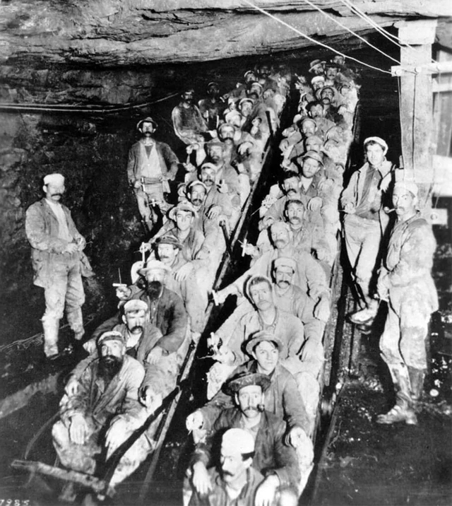 Archival photograph: miners crowded on an ore-car train underground, nineteenth century.