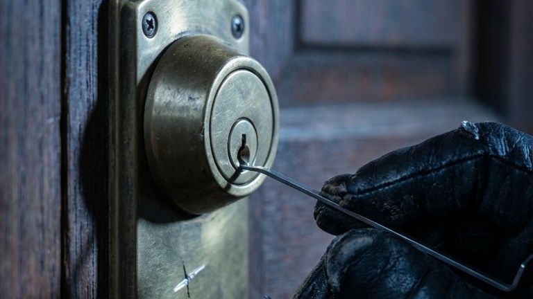 A gloved hand working a tension wrench into a brass deadbolt.