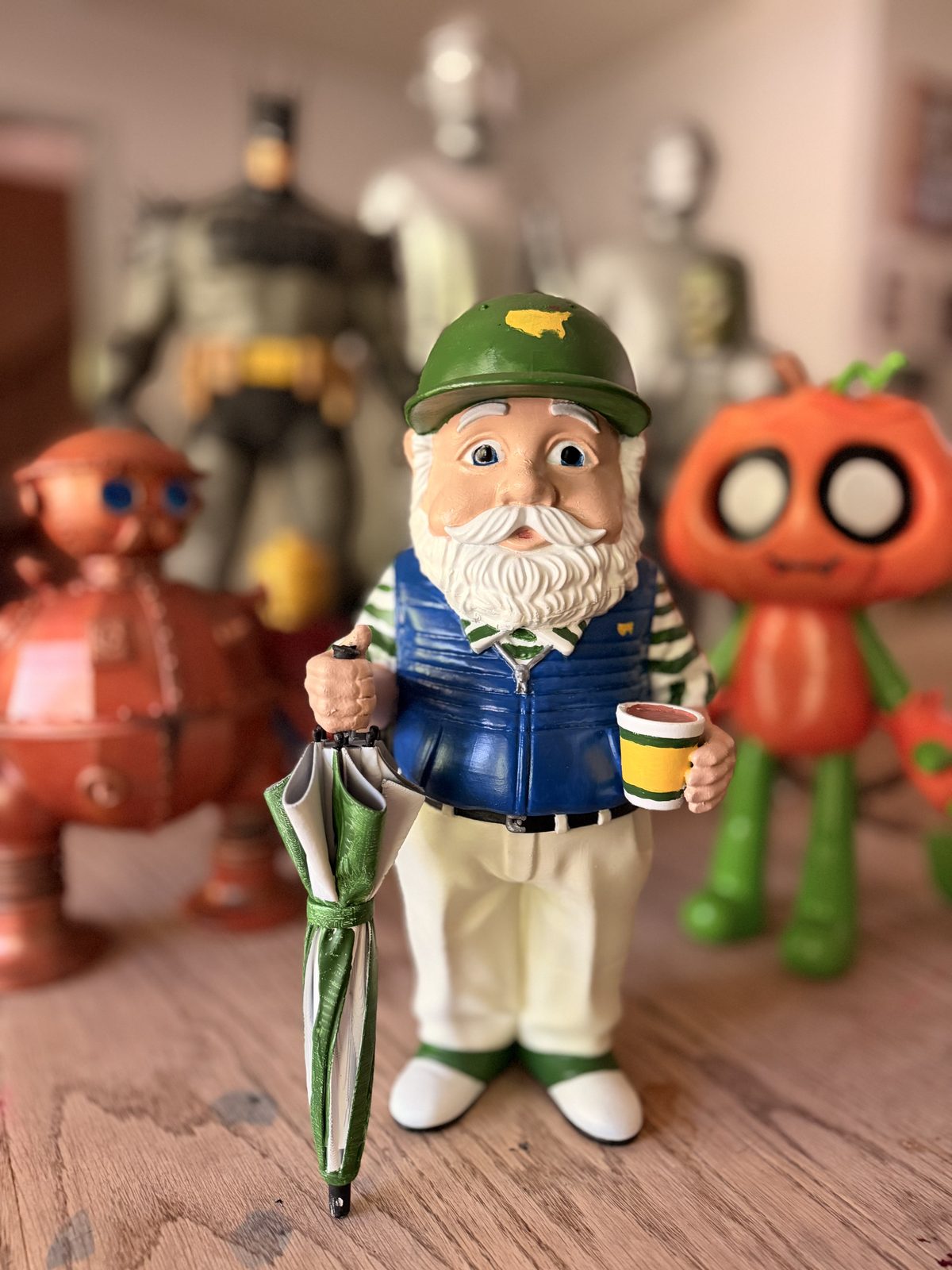 Garden gnome with green helmet, white beard, blue vest, holding a coffee cup and umbrella.
